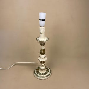 May include: A white and gold table lamp with a white lampshade and a black band around the base of the shade. The lamp has a decorative base with a green and gold design.