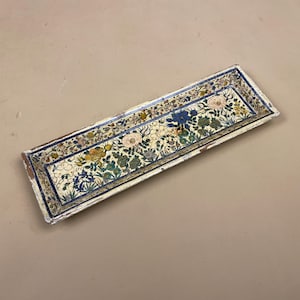 May include: A rectangular decorative tray with a floral design. The tray has a cream base with a detailed pattern of flowers in pink, blue, yellow, and green. The edges are outlined in blue and gold, adding a touch of elegance.