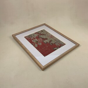 Pode incluir: Uma pe&ccedil;a de arte emoldurada com um design estampado em vermelho, branco e cinza. A moldura &eacute; de madeira e tem um acabamento marrom claro.