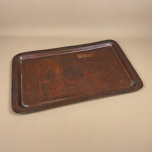 May include: An antique copper tray with etched patterns. The rectangular tray has a dark brown patina and detailed floral and geometric designs. The edges are slightly raised, and the overall aesthetic is vintage and decorative.