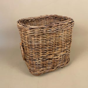 May include: A rectangular wicker basket with a rounded top, woven from light brown wicker. It features a handle on one side. This basket is suitable for storage or decorative purposes, with a rustic aesthetic.