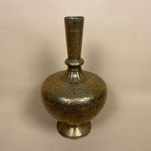 May include: A large, ornate brass vase with intricate floral designs etched into the surface. The vase has a wide, round body and a tall, slender neck.