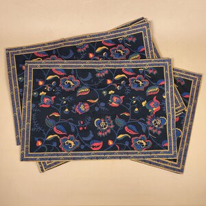 May include: Four rectangular placemats with a dark navy background and a floral design. The pattern includes blue, red, and yellow flowers and leaves. Each placemat has a gold border and a blue and gold patterned trim.