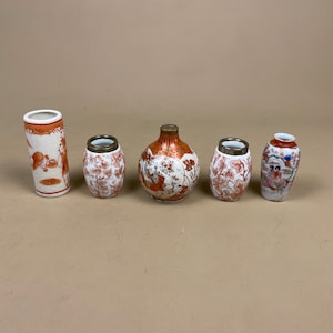 May include: A collection of five antique ceramic vases. The vases are in various shapes and sizes, with a colour scheme of white, orange, and gold. Some vases feature detailed illustrations of figures and floral patterns, while others have a simple design.