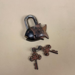May include: A black and brown fish-shaped padlock with two matching keys. The padlock has a silver shackle and the keys are ornate.