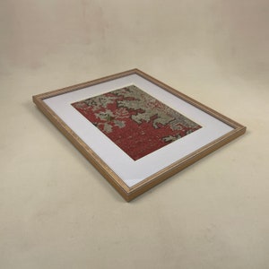 Pode incluir: Uma pe&ccedil;a de arte emoldurada apresentando um tecido estampado em vermelho e branco com um passe-partout bege e uma moldura de madeira clara.