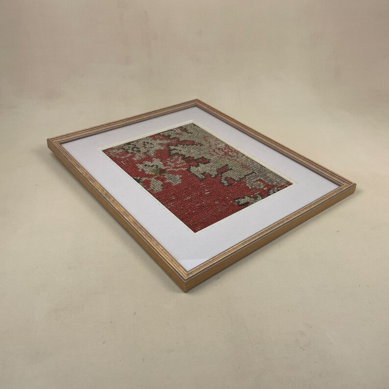 Pode incluir: Uma pe&ccedil;a de arte emoldurada apresentando um tecido estampado em vermelho e branco com um passe-partout bege e uma moldura de madeira clara.
