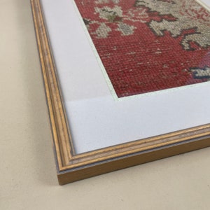Pode incluir: Uma pe&ccedil;a de arte emoldurada com um design estampado em vermelho, branco e verde. A moldura &eacute; de madeira marrom clara com acabamento dourado.