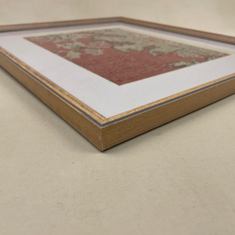 Pode incluir: Uma obra de arte emoldurada com um design de padr&atilde;o vermelho e branco. A moldura &eacute; feita de madeira clara com uma veia sutil.