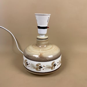 May include: A ceramic table lamp with a brown and white glazed finish. The lamp base features a floral design with brown and white accents. The lamp has a white socket and a white cord.