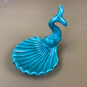 May include: A turquoise ceramic decorative dish shaped like a swan or bird. It has a curved neck and tail, with a fan-shaped base. The glossy finish and vibrant colour make it a striking decorative piece. The dish measures approximately 25 cm in length.