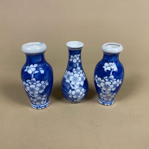 May include: Three blue and white ceramic vases with a floral pattern. The vases have a white rim and a dark blue body with white flower designs. The vases are of varying heights and shapes.