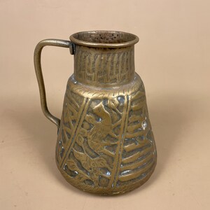 May include: A vintage brass jug with a handle. The jug features an embossed design of birds and floral patterns. The brass has a warm, aged patina, and the jug's shape is slightly bulbous, with a narrow neck and a wide base.