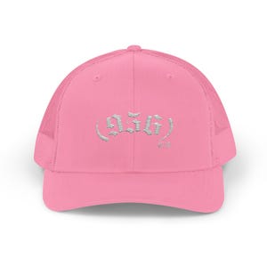 May include: Pink trucker hat with a mesh back and a curved brim. The hat features the text "555" in a stylized, silver font on the front. The hat is a solid pink color.