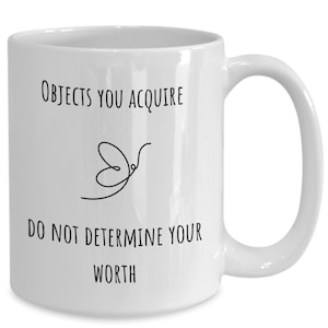 May include: White ceramic coffee mug with black text that reads "Objects you acquire do not determine your worth" and a simple line drawing of a butterfly.