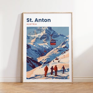 May include: Framed art print featuring a winter landscape of St. Anton, Austria. The artwork depicts a snow-covered mountain range with ski lifts and skiers. Text at the top reads "St. Anton AUSTRIA". The color palette includes shades of blue, orange, and white.