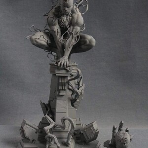 K&ouml;nnte beinhalten: Eine graue, detaillierte, 3D-gedruckte Figur eines Superhelden-Charakters mit einem schwarzen, organisch aussehenden Anzug. Die Figur ist in einer hockenden Position auf einer zerst&ouml;rten Steinplattform platziert. Die Plattform ist von zerbrochenen Steinbruchst&uuml;cken und Ranken umgeben. Eine kleinere, separate handf&ouml;rmige Figur ist ebenfalls enthalten.