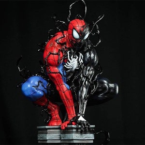 K&ouml;nnte beinhalten: Eine rote und blaue Spider-Man-Figur mit schwarzen Spinnweben wird von einer schwarzen Venom-Figur verschlungen. Die Figuren sind in einer dynamischen Action-Pose dargestellt, wobei Spider-Mans Arme ausgestreckt sind und Venoms Arme ihn umarmen. Die Figuren stehen auf einem grauen Steinsockel.