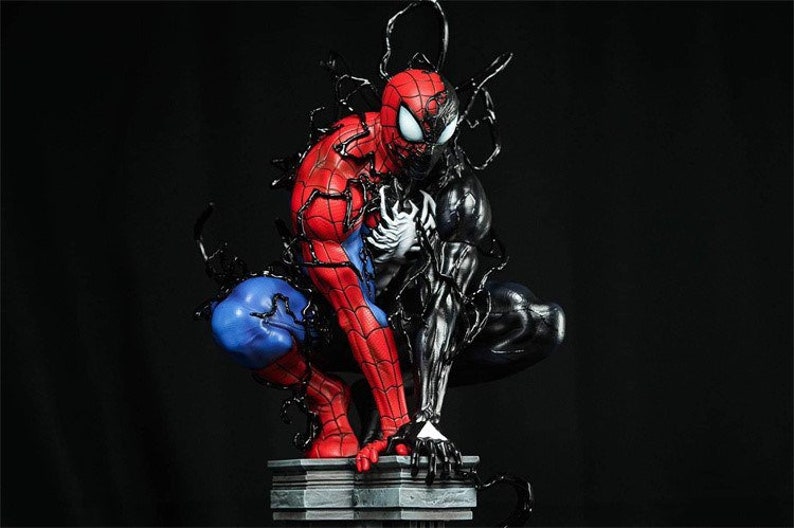 K&ouml;nnte beinhalten: Eine rote und blaue Spider-Man-Figur mit schwarzen Spinnweben wird von einer schwarzen Venom-Figur verschlungen. Die Figuren sind in einer dynamischen Action-Pose dargestellt, wobei Spider-Mans Arme ausgestreckt sind und Venoms Arme ihn umarmen. Die Figuren stehen auf einem grauen Steinsockel.