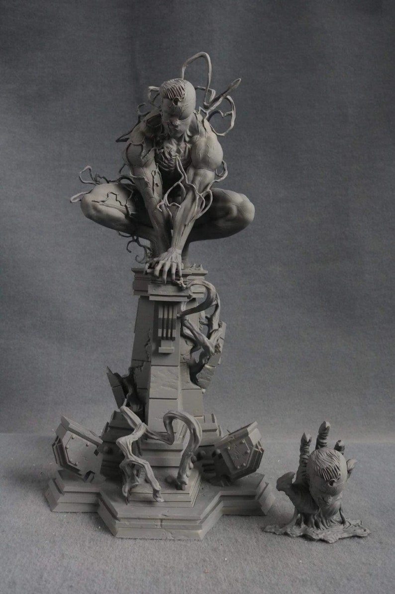 May include: A gray, detailed, 3D printed figurine of a superhero character with a black, organic-looking suit. The figure is posed in a crouching position on a ruined, stone platform. The platform is surrounded by broken pieces of stone and vines. A smaller, separate hand-shaped figurine is also included.