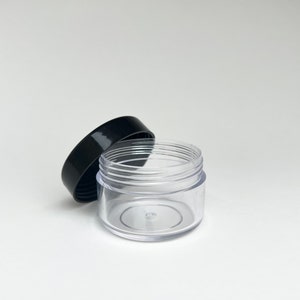 May include: A clear plastic jar with a black lid. The jar is empty and has a smooth, rounded bottom.