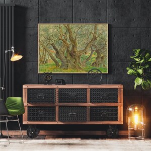 May include: A framed painting of a grove of olive trees with thick trunks and branches, set against a dark grey wall with a wooden dresser and a lamp in the foreground.