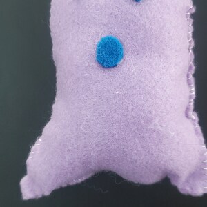 May include: A purple felt ghost with blue felt eyes and mouth. The ghost is handmade and has a stitched outline.