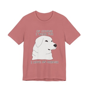 Puede incluir: Camiseta rosa polvoriento con una ilustración de un perro Akbash blanco. El texto "OF COURSE I WEAR FUR I HAVE AN AKBASH" está impreso encima y debajo de la cabeza del perro. La camiseta tiene mangas cortas y cuello redondo.