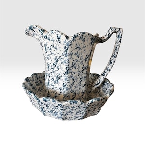 Könnte beinhalten: Ein Krug- und Beckenset aus Keramik mit weißer Basis und dunkelblauem Sprenkelmuster. Der Krug hat einen gewellten Rand und einen geschwungenen Henkel, während das Becken ein dazu passendes Design mit gewelltem Rand aufweist.