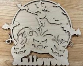 May include: A wooden Halloween decoration depicting a witch on a broomstick in front of a full moon, bats, and carved pumpkins. The word "Halloween" is cut out at the base. The decoration is made of light-coloured wood.