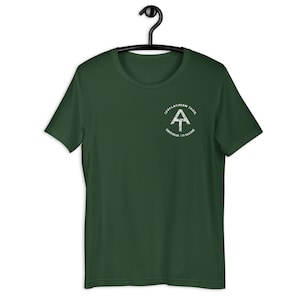 Puede incluir: Una camiseta verde oscuro con un gráfico blanco del logotipo del Sendero de los Apalaches. El logotipo incluye el texto "Appalachian Trail" y "Georgia to Maine".
