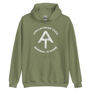 Puede incluir: Una sudadera con capucha verde con un gráfico blanco desgastado del logotipo del Sendero de los Apalaches. El logotipo incluye el texto "Appalachian Trail", un triángulo blanco con una "A" blanca en su interior, y el texto "Georgia to Maine".