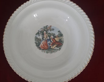 May include: A white ceramic serving bowl with a gold rim and a painted scene of a couple in a garden.