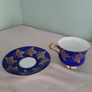 May include: A blue and gold teacup and saucer set with a vine pattern. The teacup has a gold rim and a gold handle.