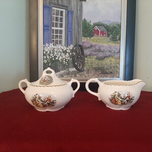 Peut inclure: Un ensemble sucrier et crémier en porcelaine blanche avec des bordures dorées et des motifs floraux. L'ensemble représente un couple dans une scène pastorale.