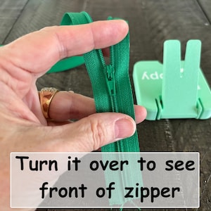 May include: A bright green zipper with a matching slider and pull tab, shown from the back side. The zipper tape is made of fabric, and the text "Turn it over to see front of zipper" is printed in black on a white rectangular overlay.