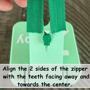 May include: A mint green plastic zipper installation tool with a central slot and a green zipper slider. The tool features white text that reads: Align the 2 sides of the zipper with the teeth facing away and towards the center.