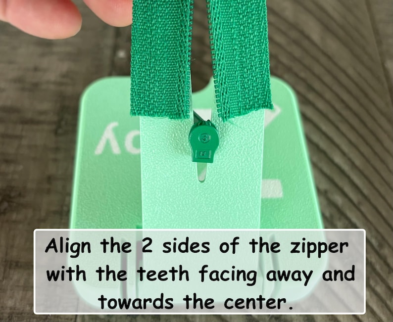 May include: A mint green plastic zipper installation tool with a central slot and a green zipper slider. The tool features white text that reads: Align the 2 sides of the zipper with the teeth facing away and towards the center.