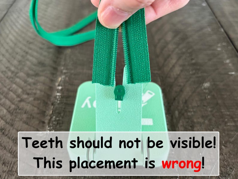 May include: A green zipper being inserted into a light green plastic tool. The text on the tool reads: Teeth should not be visible! This placement is wrong! The zipper tape is green with matching teeth, and the tool has a central slot for alignment.