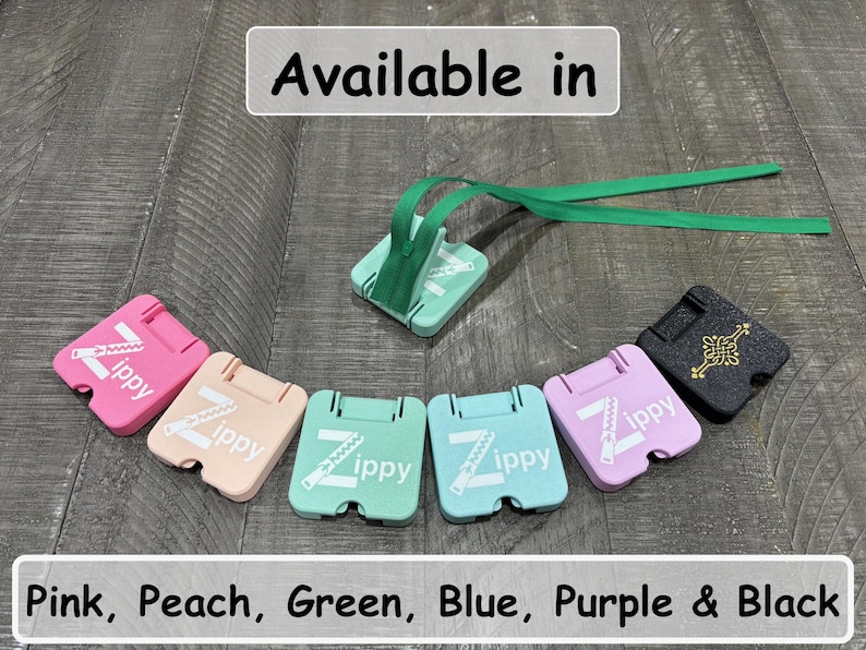 May include: A collection of square zipper pull aids in pink, peach, light green, blue, and purple, each featuring the white text Zippy and a zipper graphic. A black version features a gold Celtic knot design. One green pull includes a green ribbon.