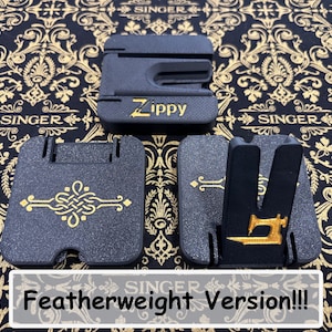 May include: Three black plastic Zippy sewing machine accessories with gold accents. One piece features the text Zippy, another has a gold decorative knot design, and the third displays a gold sewing machine icon. The items are arranged on a black fabric.