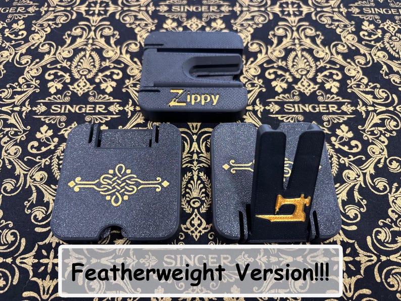 May include: Three black plastic Zippy sewing machine accessories with gold accents. One piece features the text Zippy, another has a gold decorative knot design, and the third displays a gold sewing machine icon. The items are arranged on a black fabric.