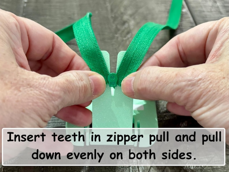 May include: A bright green zipper being threaded through a light mint green plastic zipper installation tool. The tool features a central slot for the zipper slider and includes the printed text: Insert teeth in zipper pull and pull down evenly on both sides.