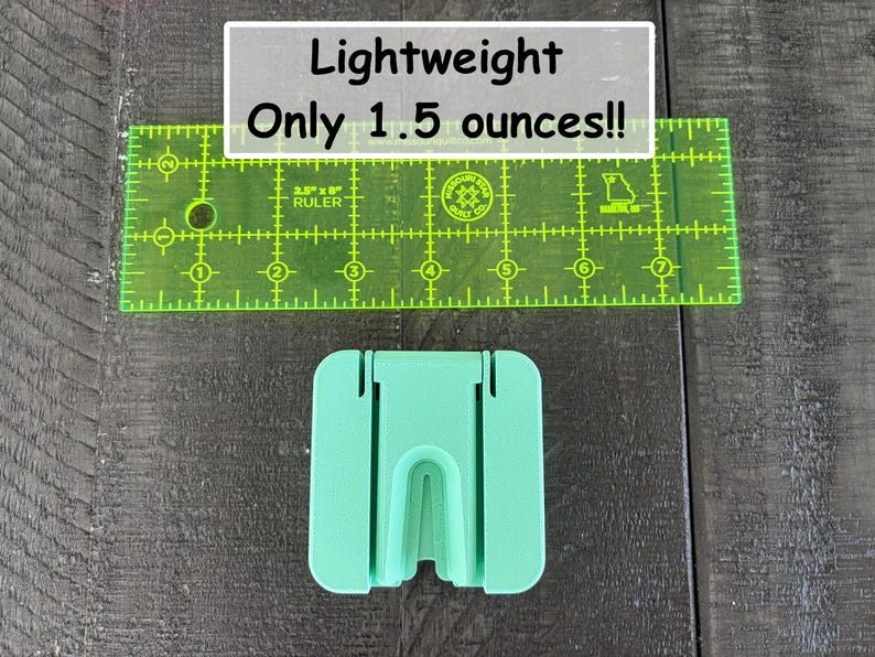 May include: A mint green plastic stand with a central U-shaped cutout, positioned below a transparent green 2.5-inch by 8-inch ruler. The text on the image reads: Lightweight Only 1.5 ounces!! The stand features a flat base and vertical slots.