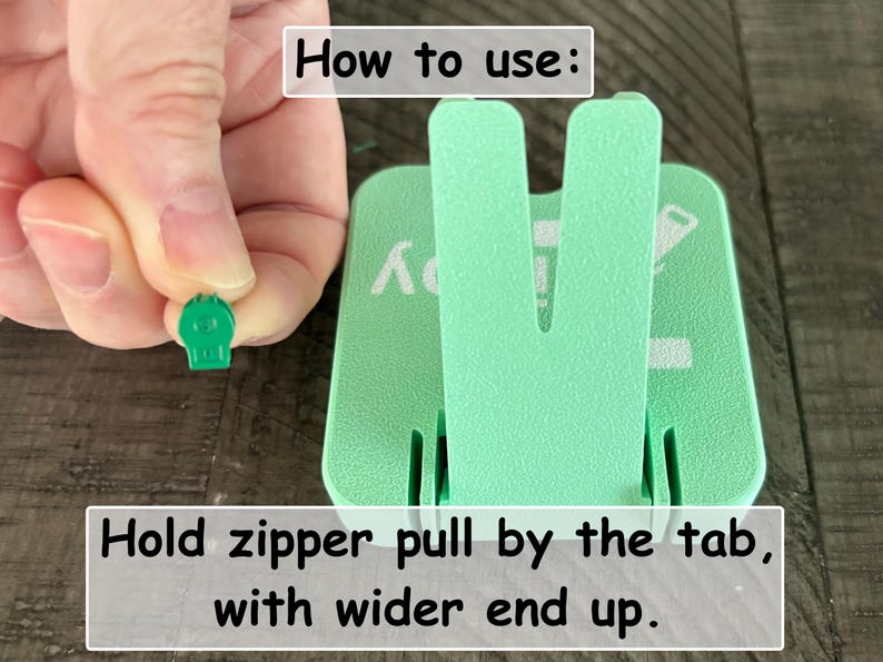 May include: A mint green plastic zipper aid tool with a V-shaped upright support. The tool features white printed text that reads How to use: and Hold zipper pull by the tab, with wider end up. A small green zipper pull is held near the tool.