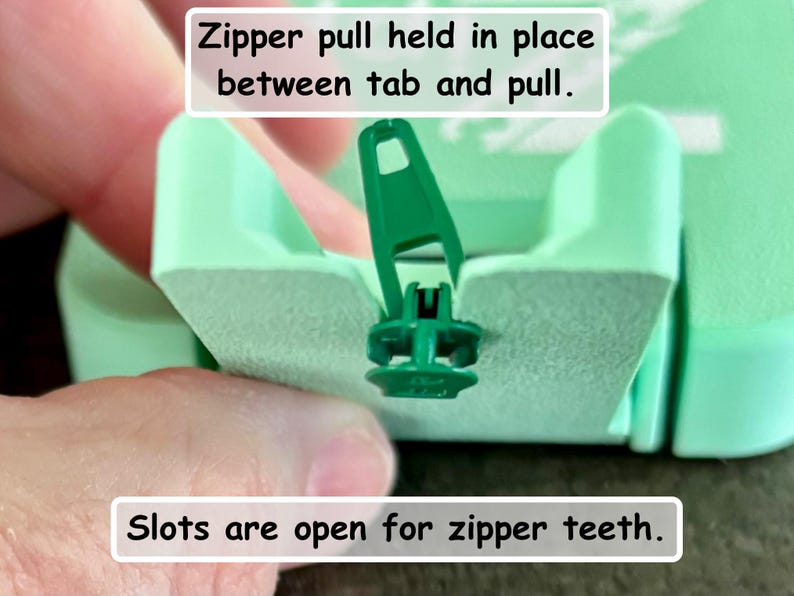 May include: A light green plastic zipper repair tool featuring a central slot for zipper teeth and a designated tab to hold the zipper pull in place. The tool includes text labels stating: Zipper pull held in place between tab and pull, and Slots are open for zipper teeth.