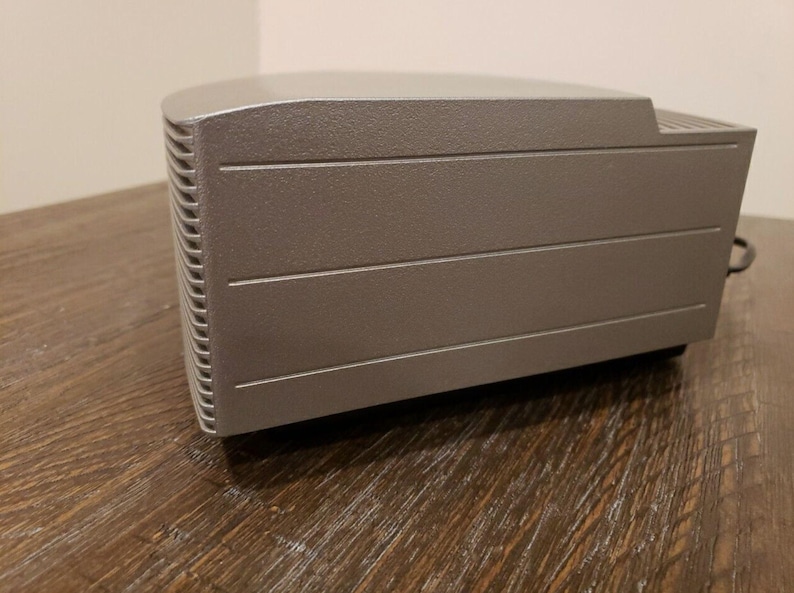 May include: A silver-colored rectangular electronic device with a textured surface and a series of horizontal lines.