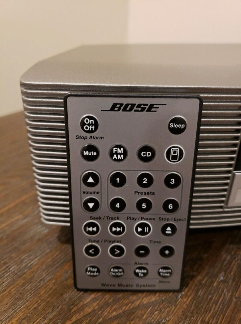 May include: A silver Bose Wave Music System with a remote control. The remote has buttons for On/Off, Sleep, Stop Alarm, Mute, FM/AM, CD, Volume, Presets, Seek/Track, Play/Pause, Stop/Eject, Tune/Playlist, Time, Alarm, Play Mode, Alarm On/Off, Wake to Alarm, and Alarm Time.
