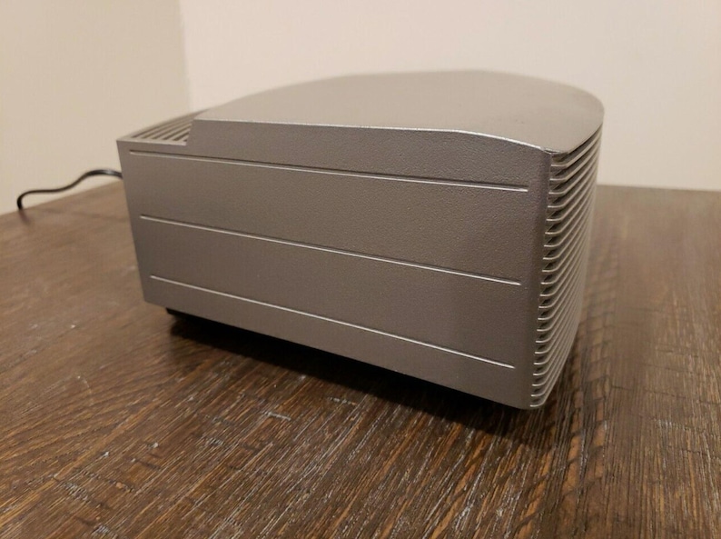 May include: A silver-colored, rectangular-shaped speaker with a slightly curved top and a textured, ribbed side panel.