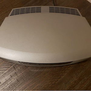 May include: A silver-colored DVD player with a curved design and a slot for a disc on the front.